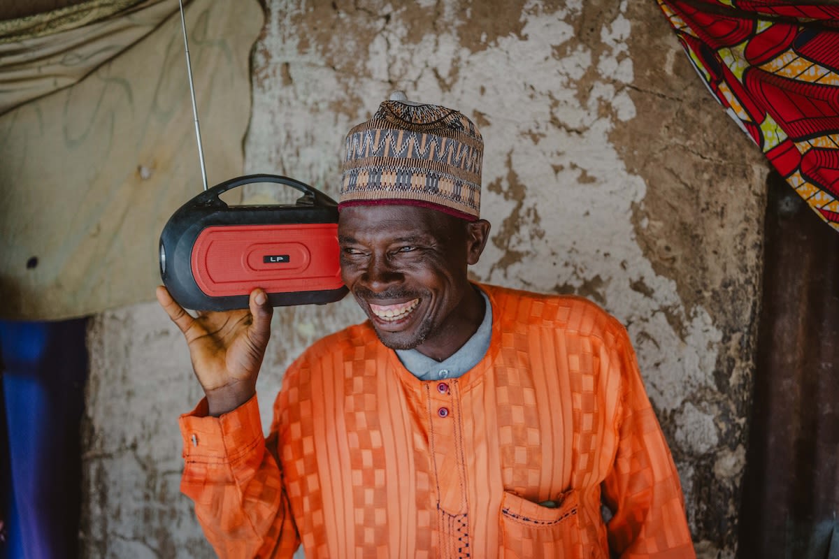 A farmer in Nigeria listens to a radio programme in front of his home